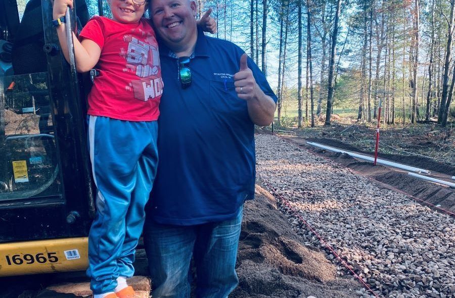 Man and child pose near construction site, man giving thumbs up.