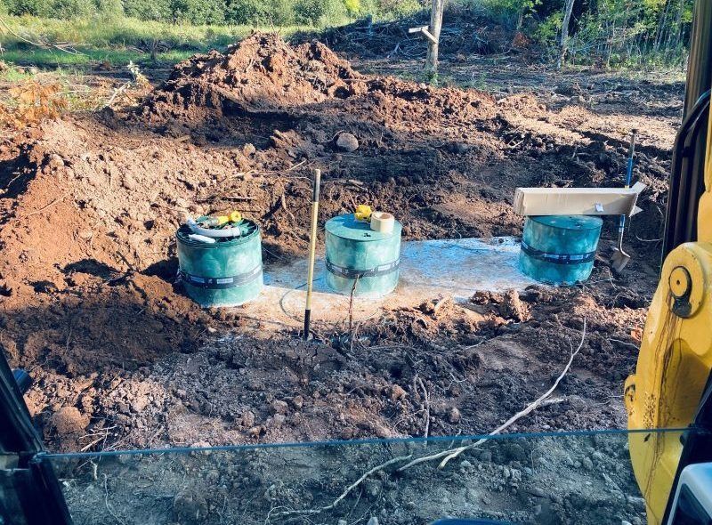 Three green septic tanks in dirt, possibly under construction, seen from excavator.