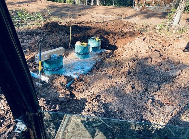 Excavation site with green septic tanks. Construction in dirt, seen from machinery window.