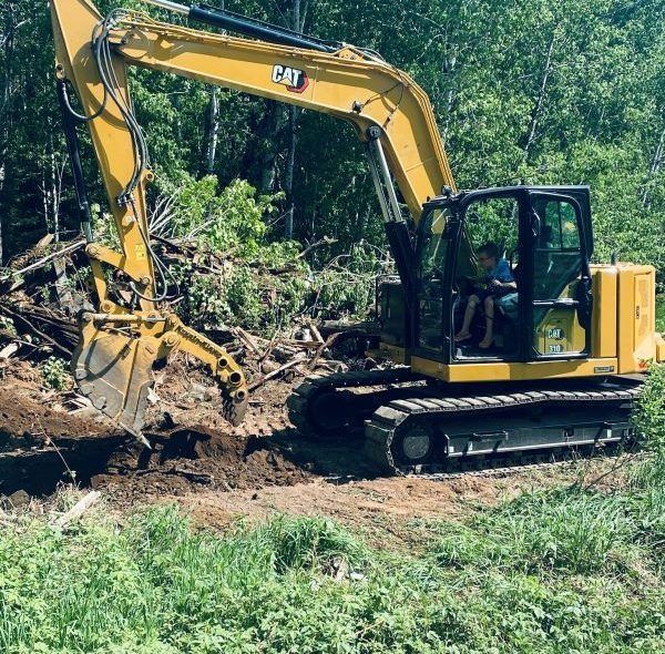Yellow Caterpillar excavator digging earth; trees in background.