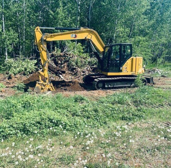 Yellow excavator digging in a field near a forest.