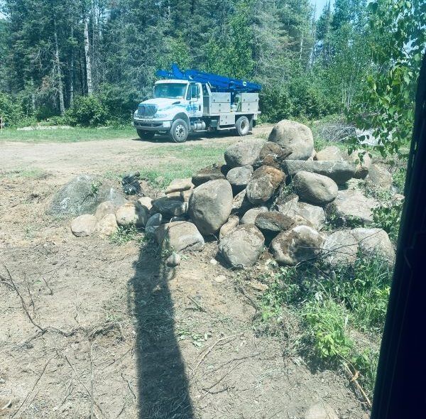 Truck parked behind a pile of rocks on a dirt road; trees in the background.