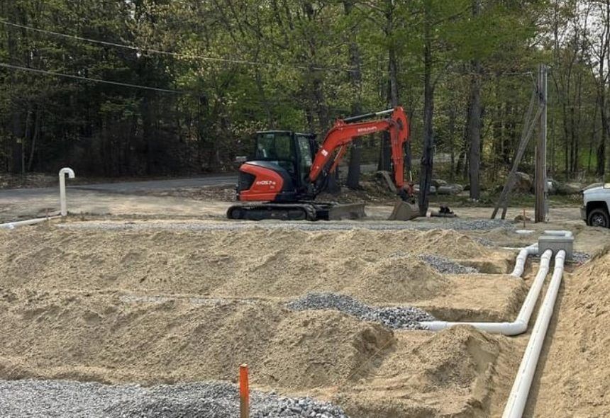 An excavator on a construction site, working near white pipes and a sandy area.