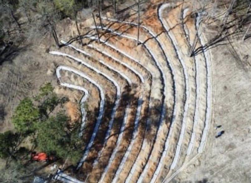 Aerial view of a hillside with terraced erosion control barriers, showing earthworks with white fabric.