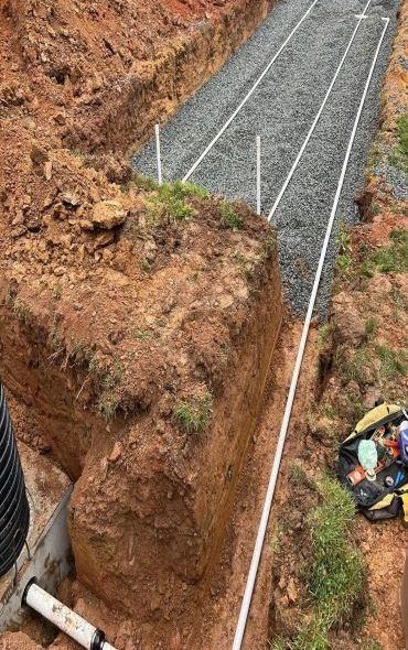 A trench dug for a septic system with gravel, pipes, and exposed earth, outdoors.