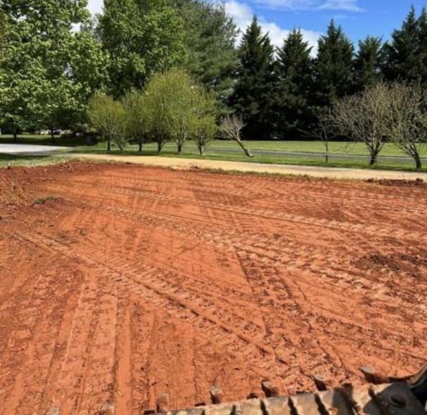 Cleared red dirt lot with tire tracks, trees in background.