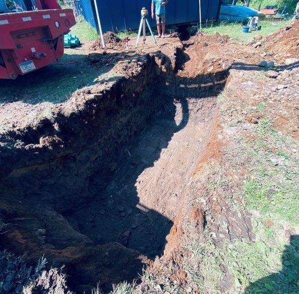 A deep trench dug in the earth with equipment and people in the background.