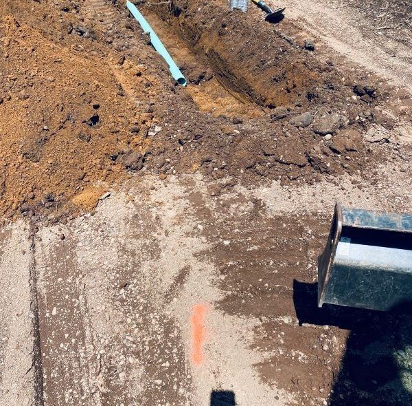 A construction site with a trench, blue pipe, and heavy machinery.