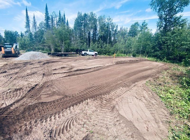 Dirt track with tire tracks, construction equipment, and a truck in a wooded area.