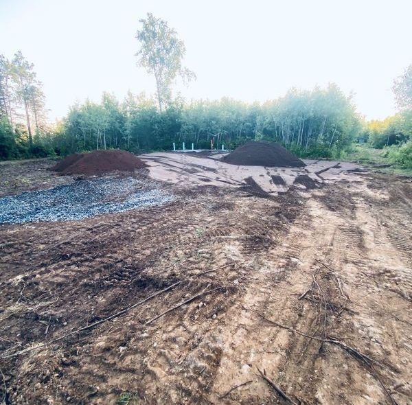Dirt piles on a cleared construction site, trees in the background.