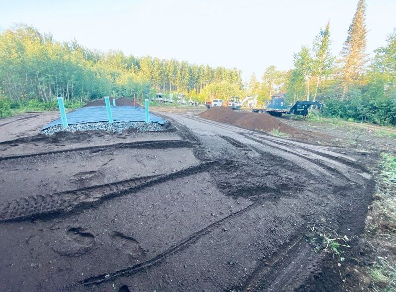 Construction site with dirt tracks, green posts on concrete, and a forest backdrop.
