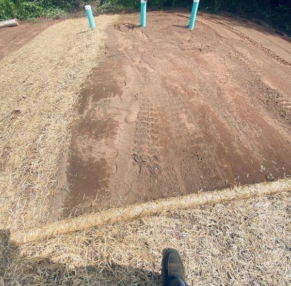 Dirt area with straw erosion control, blue pipes, and tire tracks.