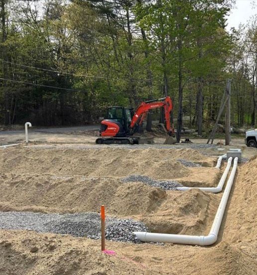 An excavator sits on a sandy lot, installing white pipes.
