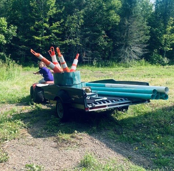 ATV with traffic cones and PVC pipes in a field. Person driving. Green grass and trees in the background.