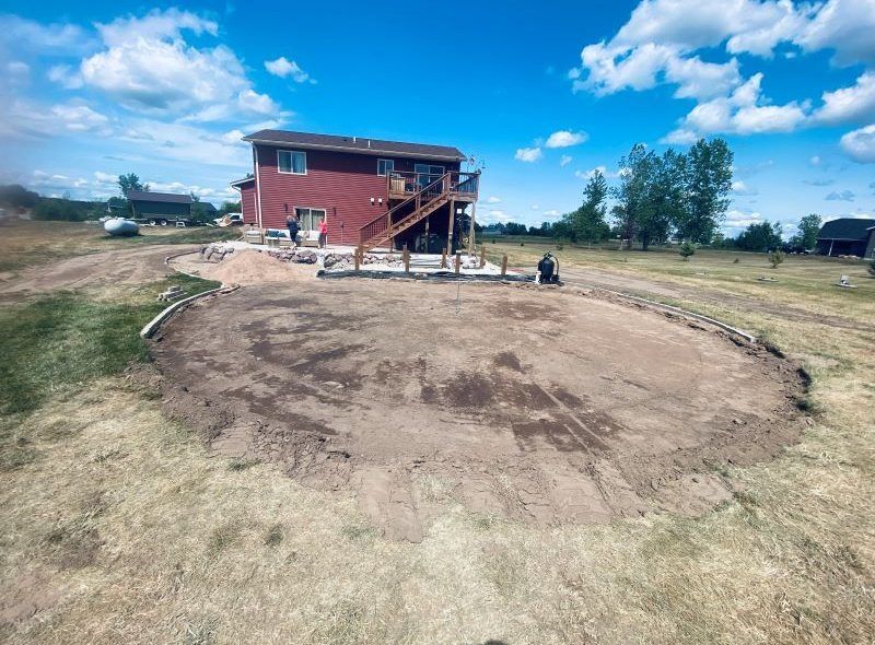 Backyard with a house, dirt area for landscaping, and a blue sky.