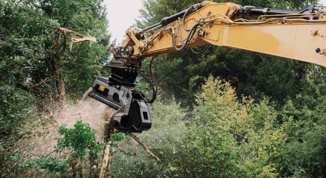 Yellow excavator with a grinding attachment shredding a tree.