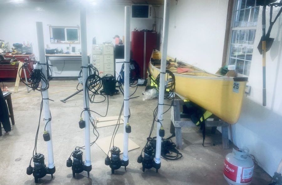Four sump pumps with PVC pipes in a garage; a canoe and person in the background.
