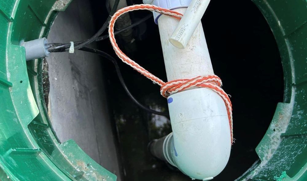 Open septic tank with green lid, showing PVC pipe, rope, and wiring.