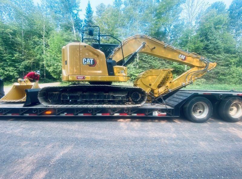 Yellow Caterpillar excavator on a trailer, ready for transport, parked on a road.