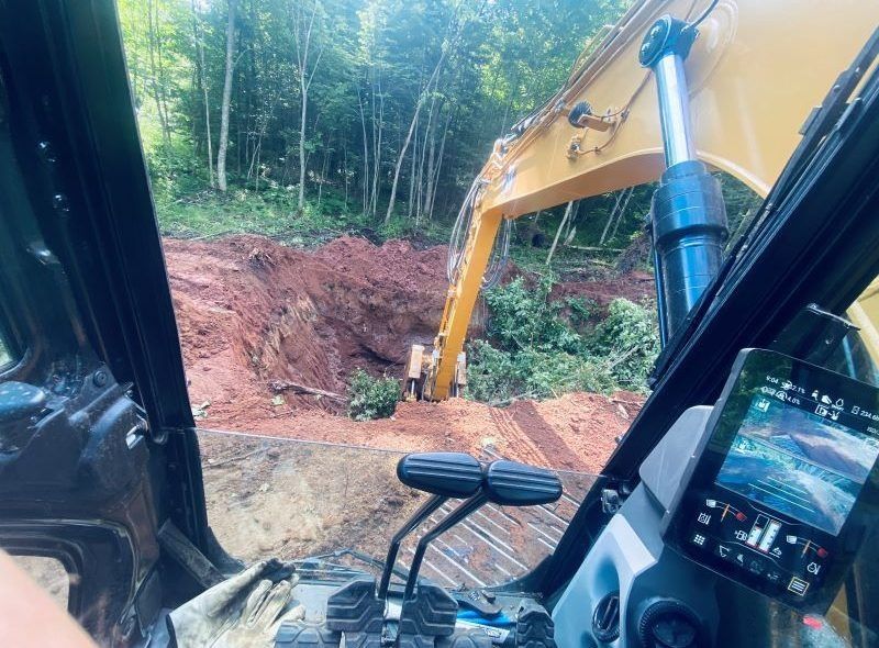 Interior view of an excavator operating near a dirt bank and trees.