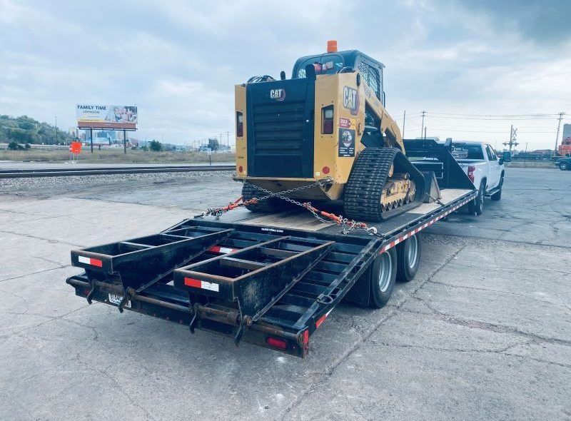 A yellow Caterpillar track loader secured on a flatbed trailer, ready for transport, outdoors.
