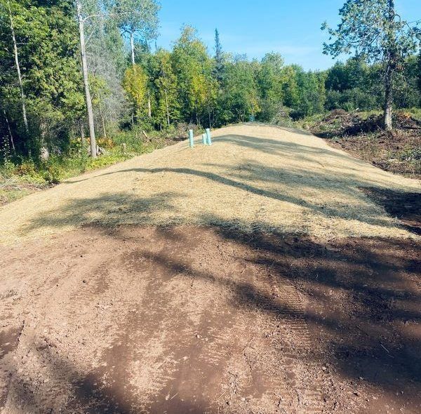 Brown, grassy hill with blue pipes in a forest clearing under a blue sky.