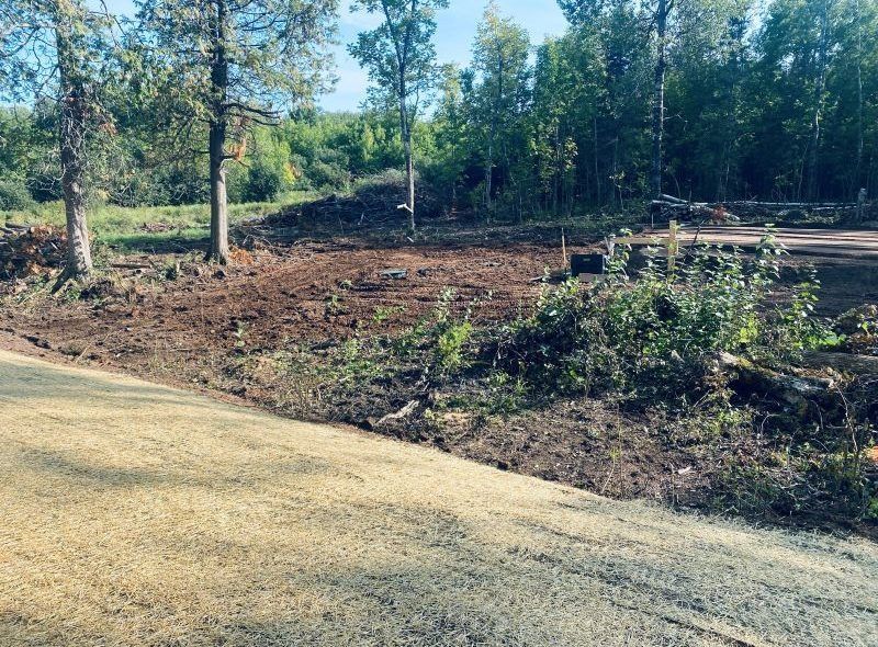 Cleared land with brown soil, trees in the background, and a grassy area in the foreground.
