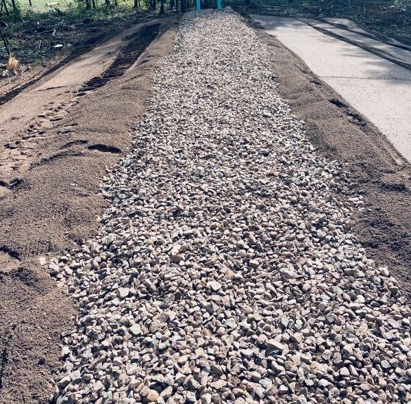 Gravel and dirt path between asphalt road sections; blue pipes in the distance.