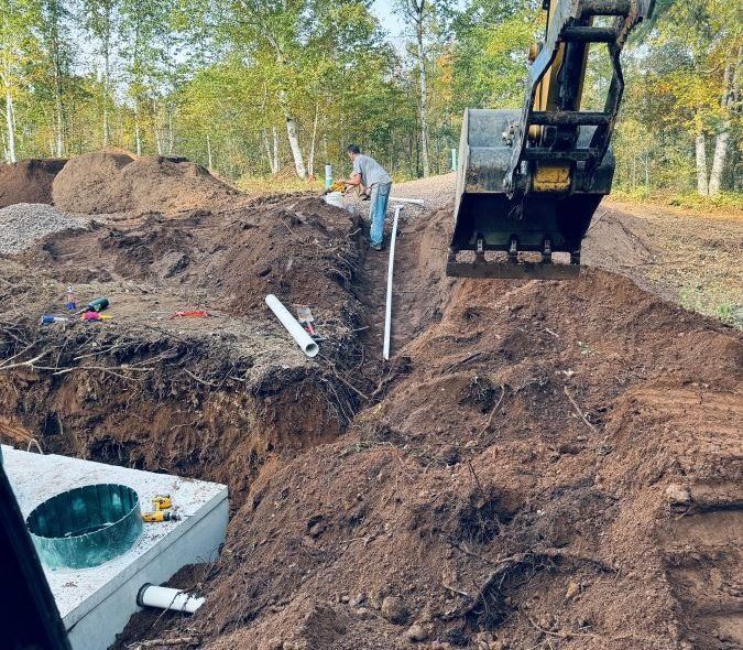 Construction worker installing pipe in trench near excavator. Forest background.