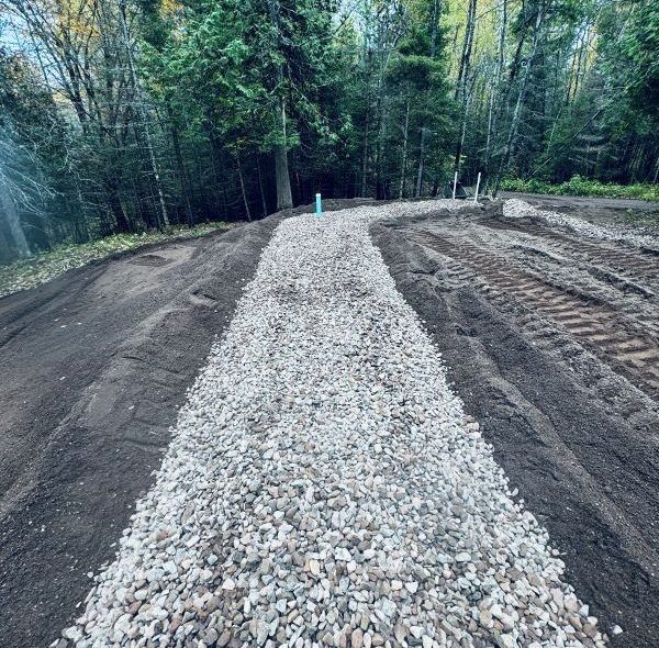 Gravel pathway through a wooded area, surrounded by dirt and construction work.