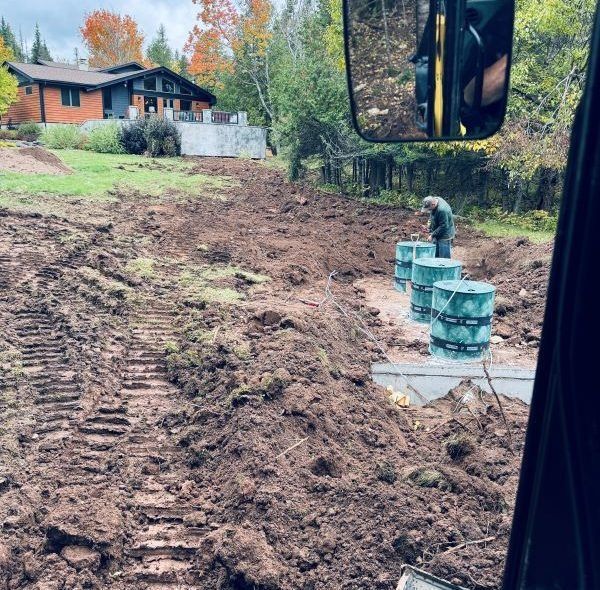 Earth moving equipment digging near a house. A person works on installing septic tanks.