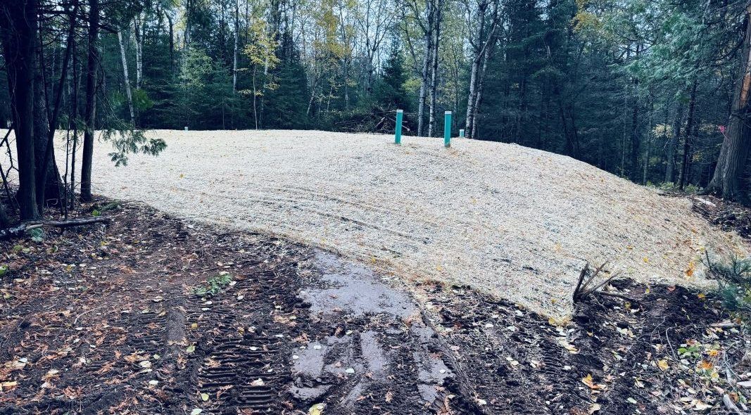 Gravel mound with two green pipes set amidst a forest. Brown and green colors.