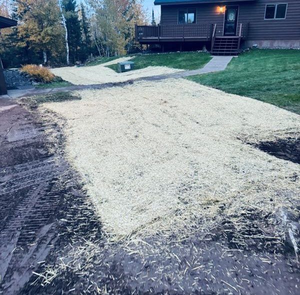 Dirt driveway covered in straw, leading to a house with dark brown siding.