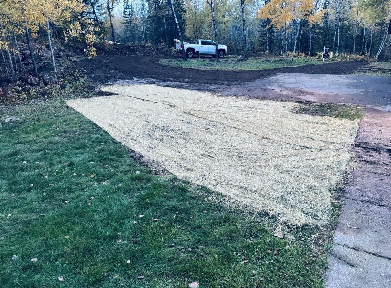A lawn area covered in hay, with a truck, trees, and driveway in the background.