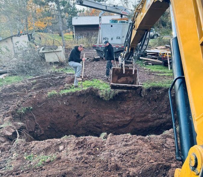 Two men digging in a large dirt pit with an excavator, outdoors.