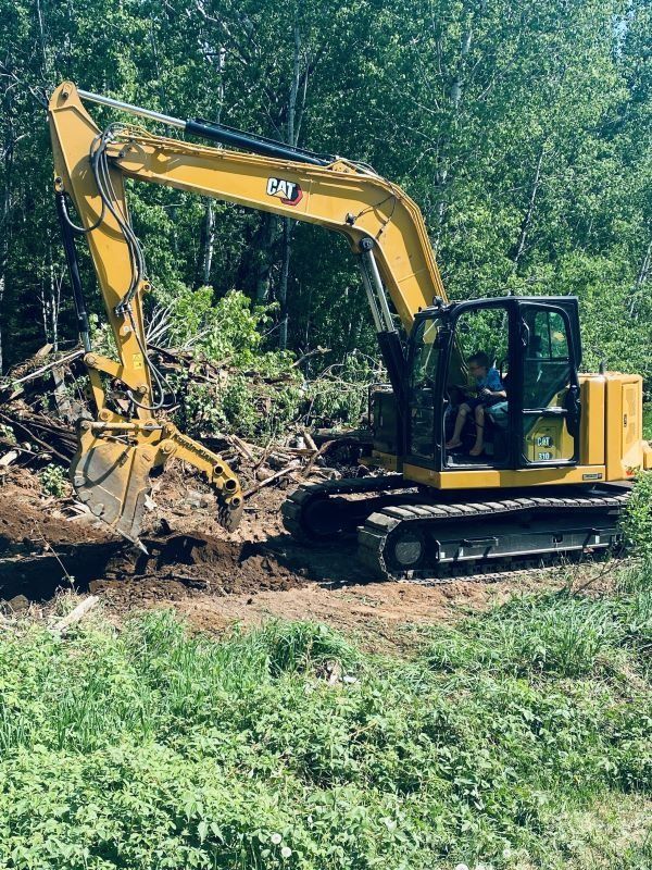 Yellow Caterpillar excavator digging in a grassy area near trees.