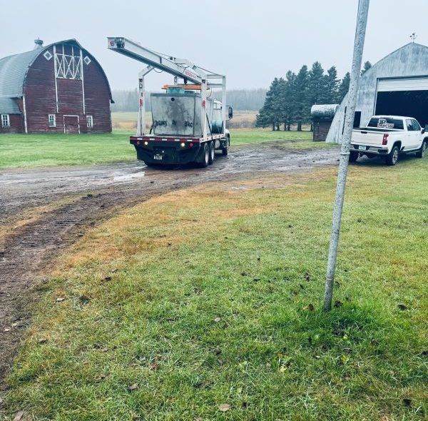 A truck with an arm on a muddy farm path, near a red barn and white truck.