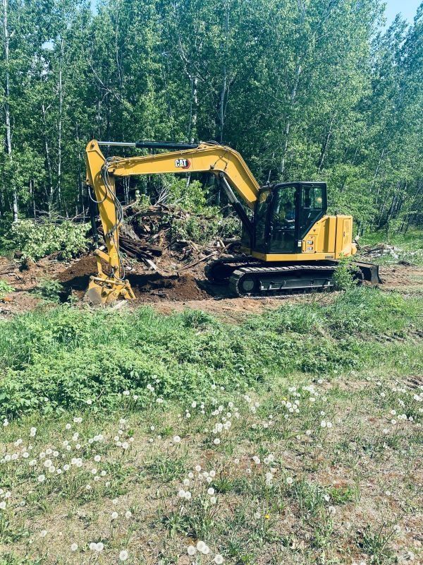 Yellow excavator digging in a dirt pile near a wooded area.