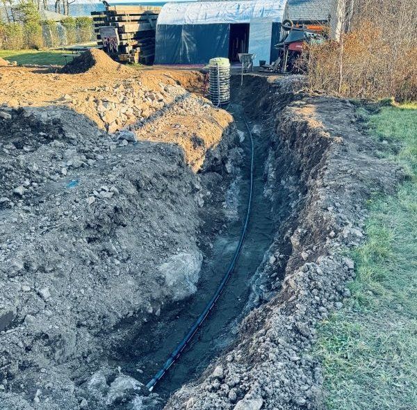 Trench in a yard, a black pipe laid in the trench. Construction scene.
