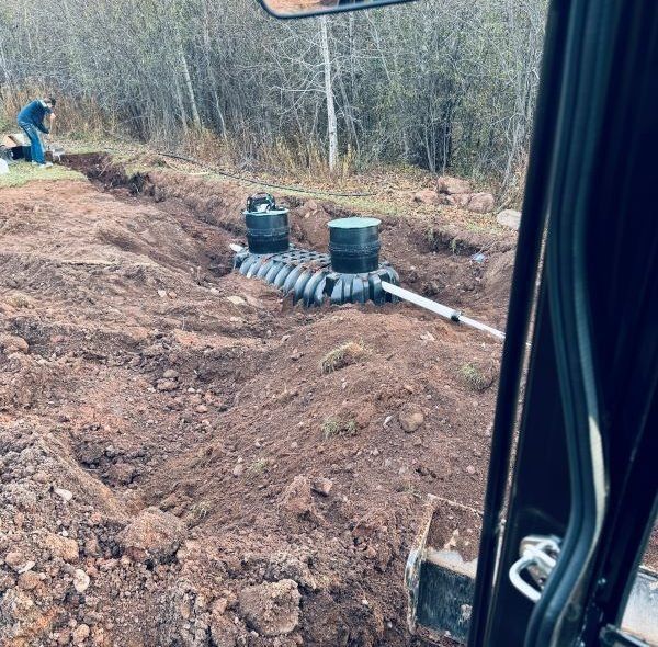 An excavator near an open trench with a septic system being installed outdoors.