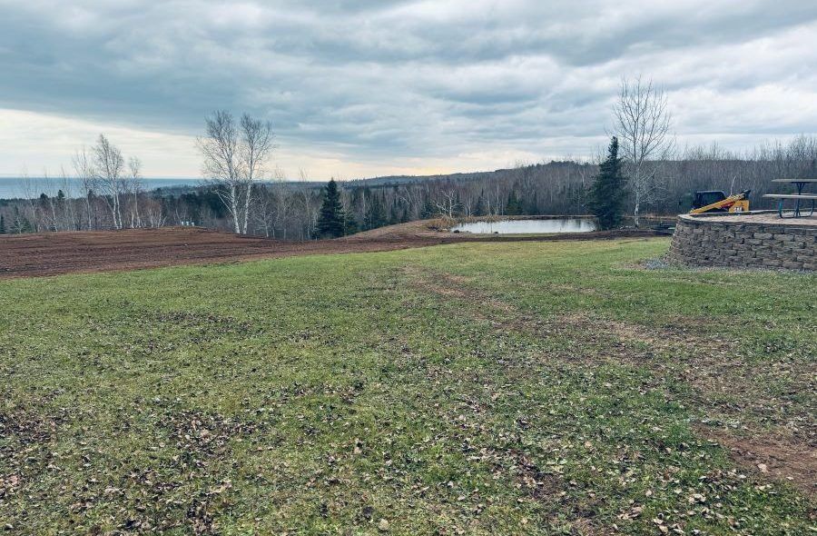 Grassy field overlooking a pond and distant water under an overcast sky.