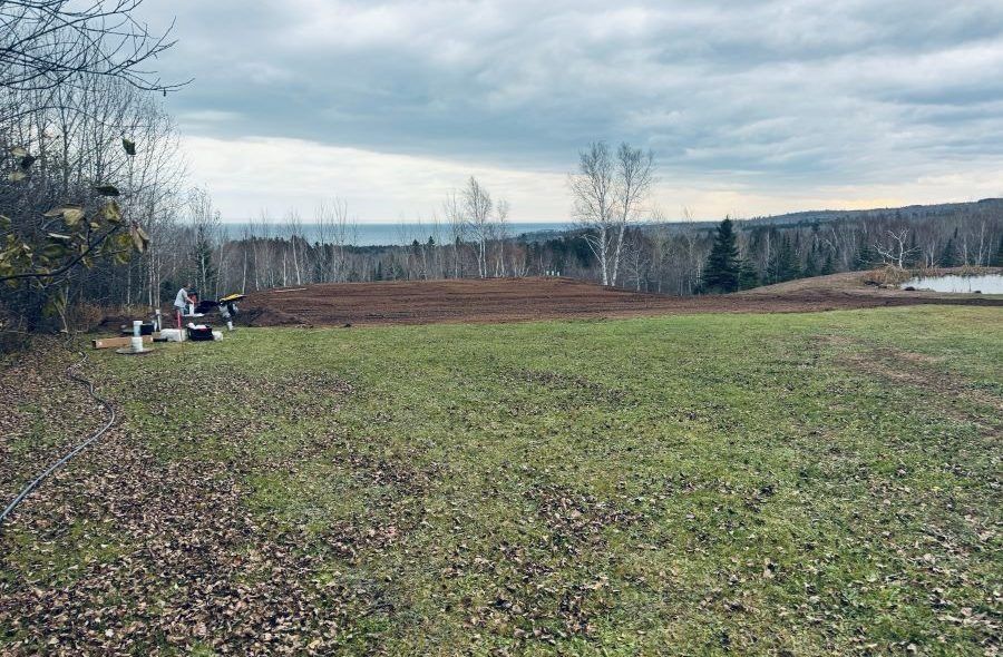 A cleared field with brown soil, overlooking a body of water, under a cloudy sky.