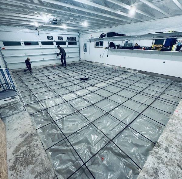 Garage floor preparation: Workers on a plastic-covered area with rebar grid, ready for concrete pour.