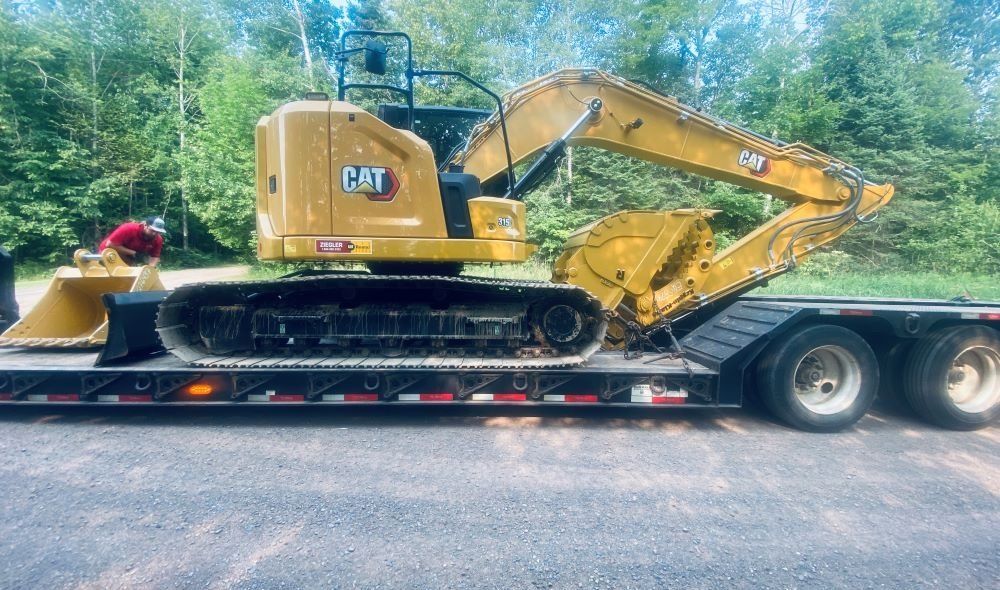 Yellow Caterpillar excavator on a black trailer, outdoors.