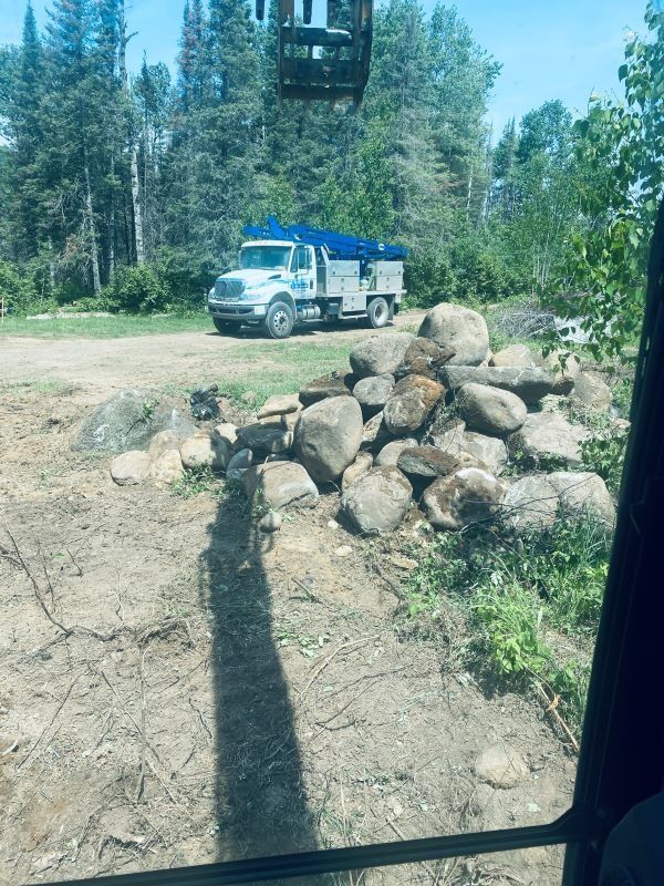A work truck parked by a pile of rocks, likely for landscaping. Green trees in background.
