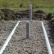 Gravel-filled trench with pipes; part of a septic system installation. Grey pipes and stone set in dirt.
