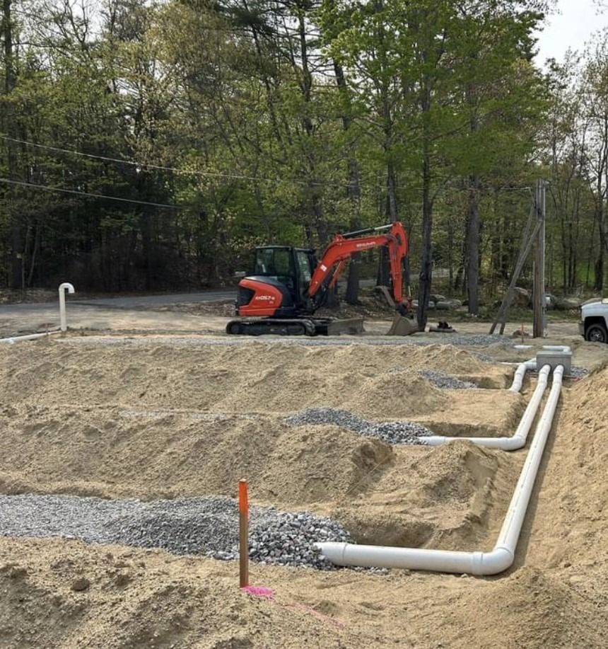 Construction site with an excavator digging near white pipes in a sand pit.