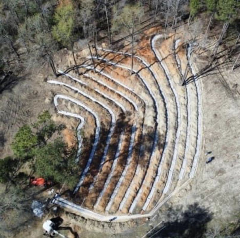 Aerial view of a newly constructed outdoor amphitheater with tiered seating and white protective barriers.
