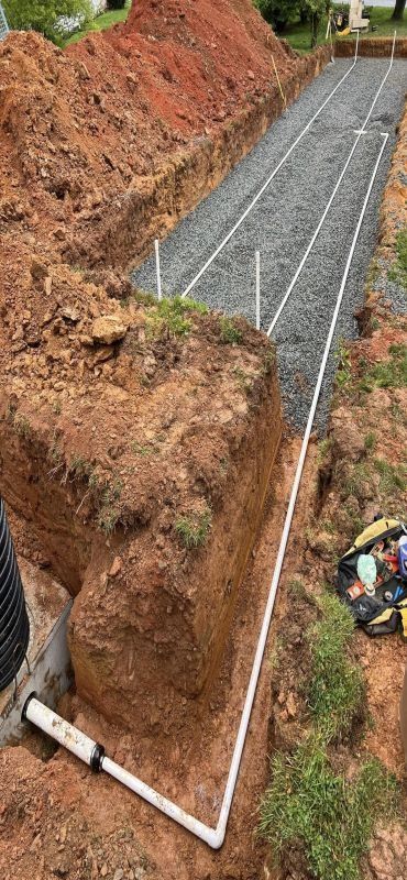 A trench filled with gravel, marked with white pipes, for a septic system installation in a yard.