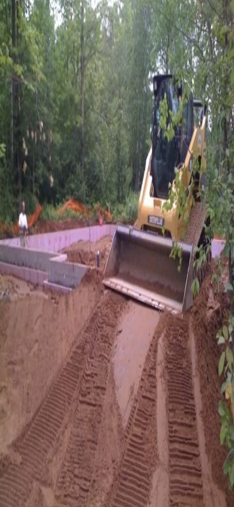 A yellow skid steer loader excavates dirt at a construction site near a forest.
